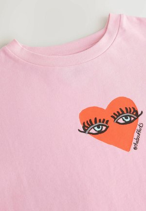 Roosa puuvillane T-särk, millel on suurte siniste silmade graafika mustade ripsmete ja oranži südamekujuga. Ümar kaelus, pehme tekstuur.