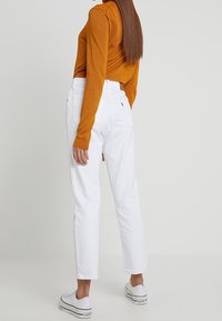 Pantalones de mezclilla blancos con un corte recto, combinados con una camiseta de manga larga naranja. Las zapatillas cuentan con detalles negros y una suela blanca.