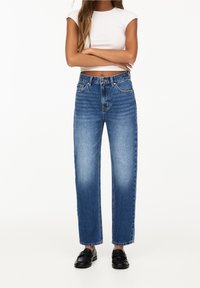 Högmidjade raka jeans i ljusblå denim. Har blekta områden och klassisk femficksdesign, tillsammans med svarta loafers.