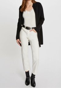 Svart zip-up jacka över en vit åtsittande topp, parat med ljusa jeans och svarta ankelstövlar. Noterbara silverfärgad spänne bälteaccenter.