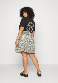 T-shirt preta de mangas curtas com gráfica branca e dourada, combinada com uma saia de estampado floral em cores pastel e um cós elástico. Sandálias pretas.