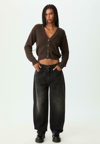 Cardigan côtelé marron avec un décolleté en V profond et cinq boutons, associé à un jean noir à taille haute et à jambes larges, ainsi qu'à des chaussures à plateforme noires.