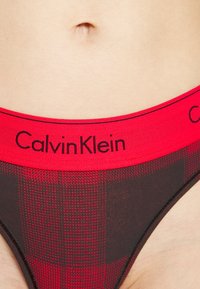 Pánske boxerky s červeným a čiernym kockovaným vzorom, širokým elastickým pásom s nápisom "Calvin Klein" vytlačeným čiernym písmom. Textúrovaná látka.