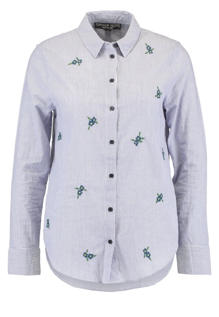 Pruhovaná modrá a bílá košile s dlouhými rukávy, zdobená květinovou výšivkou v zelené a modré barvě, a černými knoflíky vpředu.