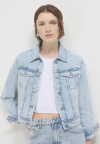 Giacca in denim blu chiaro con design classico. Presenta due tasche sul petto, accessori in argento e un taglio leggermente accorciato con una finitura testurizzata.