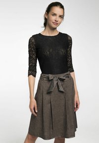 Schwarzer Spitzen-Bodysuit mit drei Viertelärmeln, kombiniert mit einem braunen plissierten Rock, der eine Schleife an der Taille und einen strukturierten Stoff aufweist.