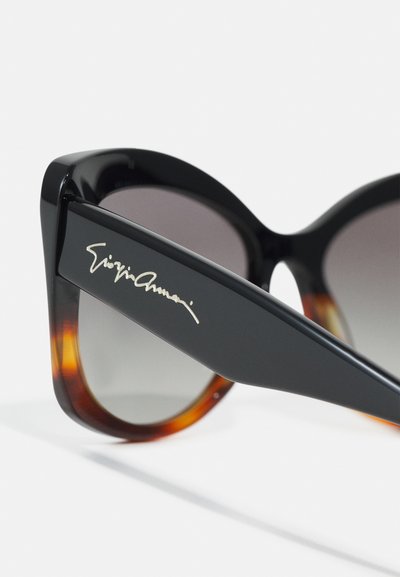 Black and tortoiseshell cat-eye sunglasses with gradient lenses and silver signature on the temple. Glossy finish and angular design.