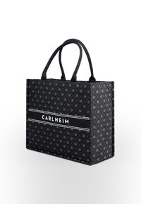 Black fabric tote bag with geometric pattern and logo. Rectangular shape with two black handles. Features white horizontal stripe with text.