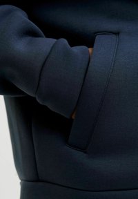 Mörkblå sweatshirt i texturerat tyg med en synlig ficka och vikta ärmslut för extra bekvämlighet. Enkel och funktionell design.