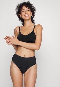 Black bralette with adjustable straps and a central gather detail, paired with high-waisted black underwear. Smooth, stretchy material.