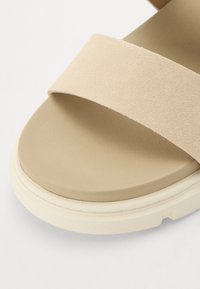 Beige semskede sandaler har et bredt stroppdesign og en myk, polstret såle med en lysfarget teksturert yttersåle.