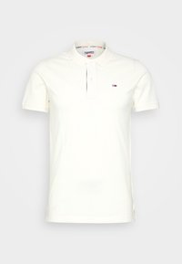 Polo en algodón color blanco roto, con un cuello clásico, tapeta de botones y un pequeño logo en el lado izquierdo del pecho. Aberturas laterales para mayor comodidad.