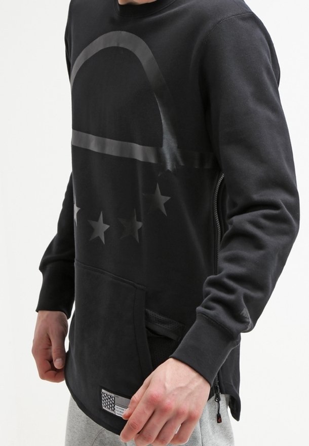 Svart sweatshirt med rund hals, med en grafisk design av stjärnor och en böjd linje över bröstet. Inkluderar en framficka och sidogångjärn.