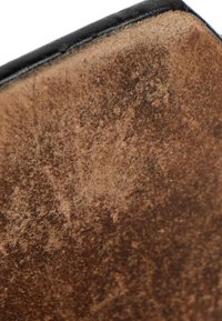 Surface en cuir marron usée avec un bord noir cousu, montrant des marques d'usure et des détails de texture.