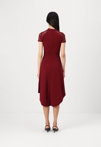 Rochie burgundy cu manșete scurte din dantelă, corset ajustat și tiv asimetric. Încheiată cu un fermoar la spate.