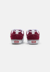 Maroon-suede tennarit, joissa on valkoisia yksityiskohtia, kumipohjat, pehmustetut kaulaukset ja valkoinen takakappale, jossa on Vansin logo. Klassinen skeittikenkätyyli.