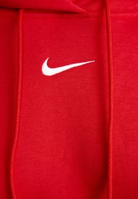 Röd bomullshoodie med en vit broderad Nike-logotyp på bröstet. Inkluderar dragsnoddar och synliga sömnadsdetaljer.