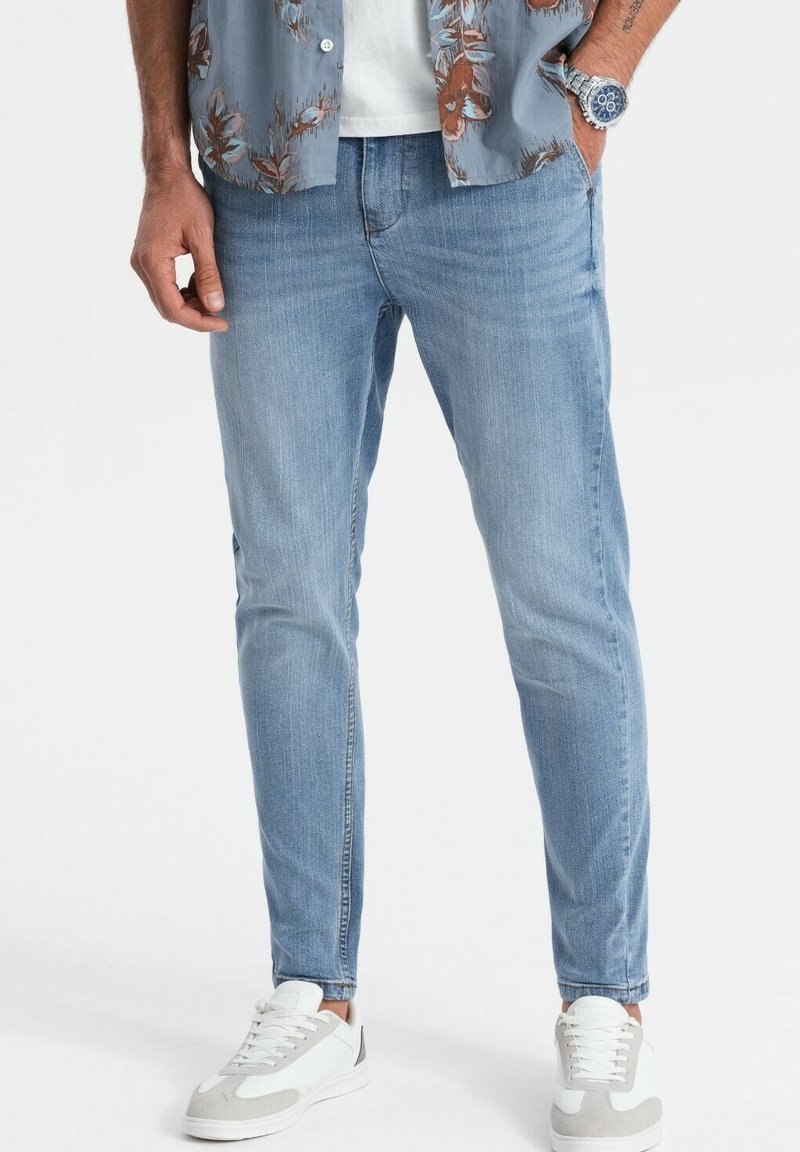 Ljust blå skinny jeans i denim med en klassisk femfickdesign, kombinerat med en mönstrad kortärmad skjorta och vita Sneakers.