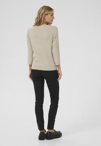 Maglione beige a costine con maniche a tre quarti, design aderente, indossato con jeans skinny neri e scarpe con plateau nere.