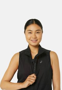 Gilet nero senza maniche con colletto rialzato, dotato di chiusura con zip e una texture sottile. Logo posizionato sul lato sinistro, con un design leggero.