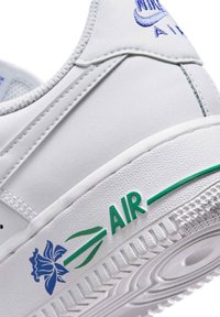 White Nike Air sneaker heel with blue flower graphic and green text "AIR" on textured white sole. Blue Nike Air logo stitched on upper heel.