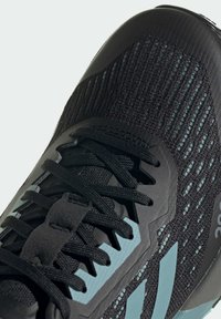 Scarpa sportiva nera con tomaia in tessuto nero testurizzato, accenti turchesi e lacci neri. Presenta un profilo slanciato e aerodinamico.