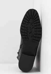 Suela de zapato negra con un patrón de relieve, que presenta profundas ranuras y diseños cruzados. Acabado liso con logotipo en el talón.