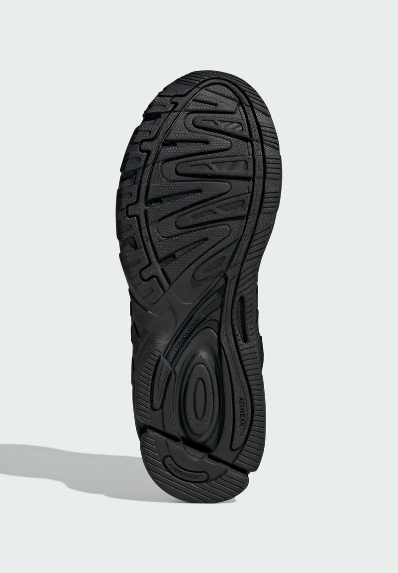 Sole di scarpe sportive nere con modelli di battistrada profondi e superfici testurizzate. Design curvo con scanalature prominenti e dettagli di branding.