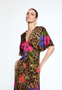 Robe de cocktail avec un décolleté en V plongeant, présentant un motif léopard agrémenté de fleurs vibrantes en rose, bleu et orange. Tissu doux et fluide.