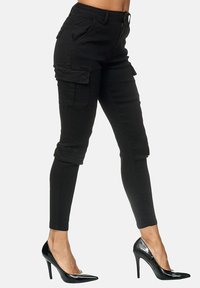 Black cargo pants with a fitted design, featuring side pockets, rolled cuffs, and a smooth texture. Paired with black high heels.