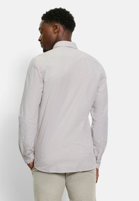 Gestreiftes Langarmhemd in hellbeige mit dünnen dunklen Streifen. Klassischer Kragen, knöpfbare Manschetten und eine lockere Passform. Glatte Textur.