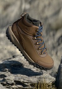 Brown waterproof hiking boot with a padded collar, blue laces, and rugged black sole. Features Columbia logo on the side.