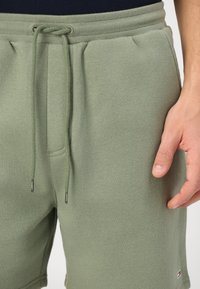 Shorts en coton verts avec une taille élastique, un cordon de serrage, des poches latérales et un petit logo en bas de l'ourlet.