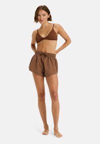 Brauner gerippter Bikini-Oberteil mit einer vorderen Schleife, kombiniert mit passenden lockeren Shorts mit elastischem Bund und sichtbaren Nähdetails.