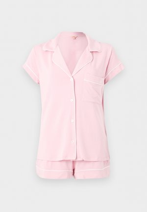 Haut de pyjama rose clair à manches courtes avec boutons, passepoil blanc et short assorti sur un fond uni.