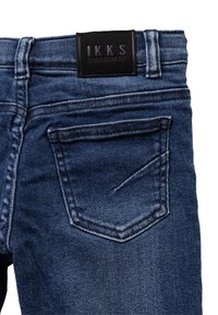 Donkerblauwe denim jeans met een leren merkpatch, vijf-pocket ontwerp en zichtbare stiksels langs de taille en zakken.