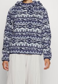 Pullover in pile blu navy e azzurro chiaro con cappuccio. Presenta disegni geometrici, maniche lunghe e un piccolo logo sul petto.
