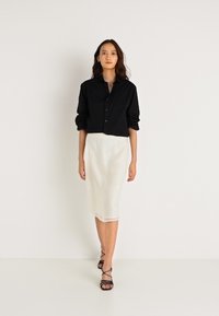 Camisa preta de botão com mangas enroladas, combinada com uma saia branca justa com detalhes sutis. Sandálias de salto pretas com tiras completam o visual.