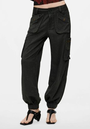 Zwarte cargobroek met hoge taille en grote voor- en zijzakken, elastische boorden, gedragen met zwarte sandalen met hak.