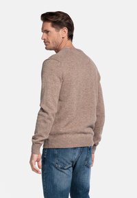 Beige gebreide trui met een ronde hals en geribde manchetten, gedragen met blauwe denim jeans. De textuur lijkt zacht en licht fuzzy.