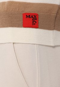 Röstripeeritud sviiter beeži, kreemi ja pruuni värviga, millel on silmatorkav punane silt, kus on musta tekstiga "MAX" allservas. Pehme tekstuur.