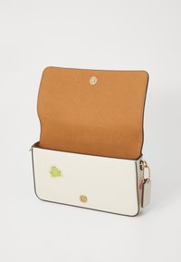 White leather bag with a brown suede interior, gold hardware, and a green frog sticker on the front. Zipper detail on the side.
