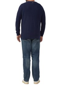 Marineblaues Langarmshirt mit strukturierter Oberfläche, Rundhalsausschnitt und lockerem Schnitt, kombiniert mit blauen Jeans und weißen Sneakern.