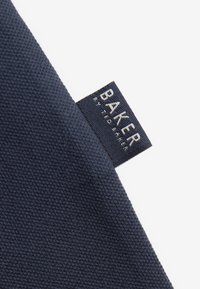 Tessuto blu scuro a trama con etichetta blu navy con testo bianco "BAKER BY TED BAKER" cucita obliquamente nella cucitura.