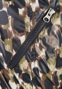 Monivärinen kangas, jossa on ruskean, vihreän ja mustan sävyjä sisältävä teksturoitu, abstrakti kuvio ja näkyvä musta vetoketju.