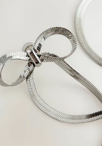 Silbernes, metallisches haaraccessoire in Form einer Schleife mit einer glatten, strukturierten Oberfläche und einem glatten zentralen Verschluss, der aus Schlaufen- und geraden Bändern besteht.