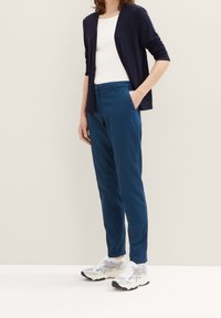 Granatowy kardigan na białej bluzce, połączony z turkusowymi spodniami. Charakteryzuje się dopasowanym krojem i bocznymi kieszeniami. Białe trampki z szarymi akcentami.