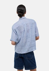 Chemise à manches courtes bleu et blanc à rayures avec une coupe décontractée, dotée d'un empiècement au dos et d'un col casual, associée à un short en denim noir.