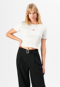 Vit ribbad kortärmad crop T-shirt med två små röda hjärtan på bröstet. Matchad med svarta höga byxor.