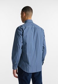 Camicia da uomo a maniche lunghe di colore blu con strisce verticali bianche e azzurre, dotata di colletto, polsini con bottoni e orlo curvo.